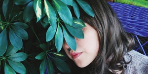 Eine Person liegt zwischen Pflanzen, ihr Gesicht wird von Blättern verdeckt.